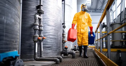 Een werknemer in een chemicaliënbestendige overall met veiligheidslaarzen ter bescherming op de werkvloer.