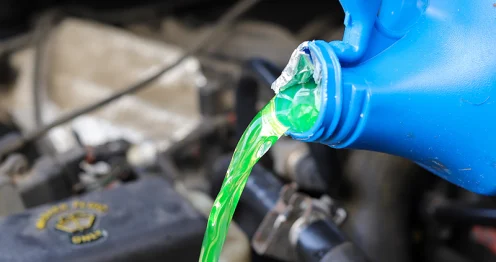 Antivries wordt gegoten vanuit een fles in het koelsysteem van een auto.