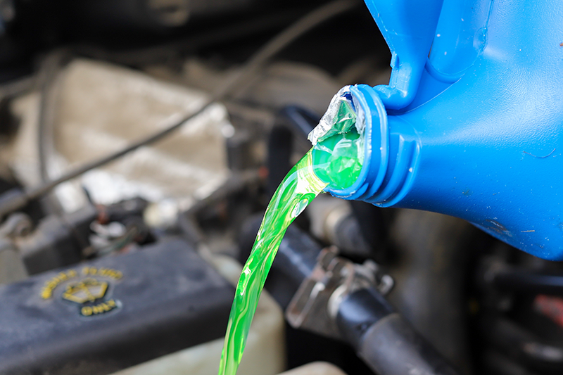 Antivries wordt gegoten vanuit een fles in het koelsysteem van een auto.