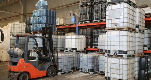 Bij deze chemische groothandel tilt een vorkheftruck gestapelde Intermediate Bulk Containers (IBC's) in een industrieel magazijn. Dit is een veelvoorkomend beeld in de chemische industrie.