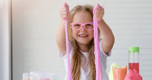 Een lachend meisje met roze bril speelt met roze slijm tijdens een wetenschappelijk experiment.