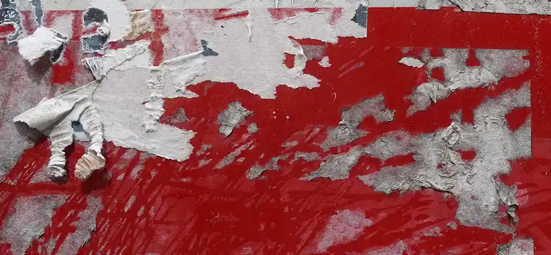 Een close-up afbeelding van hardnekkige lijmresten op een rood oppervlak, met gedeeltelijk afgescheurde en verbleekte lagen van papier en lijm.