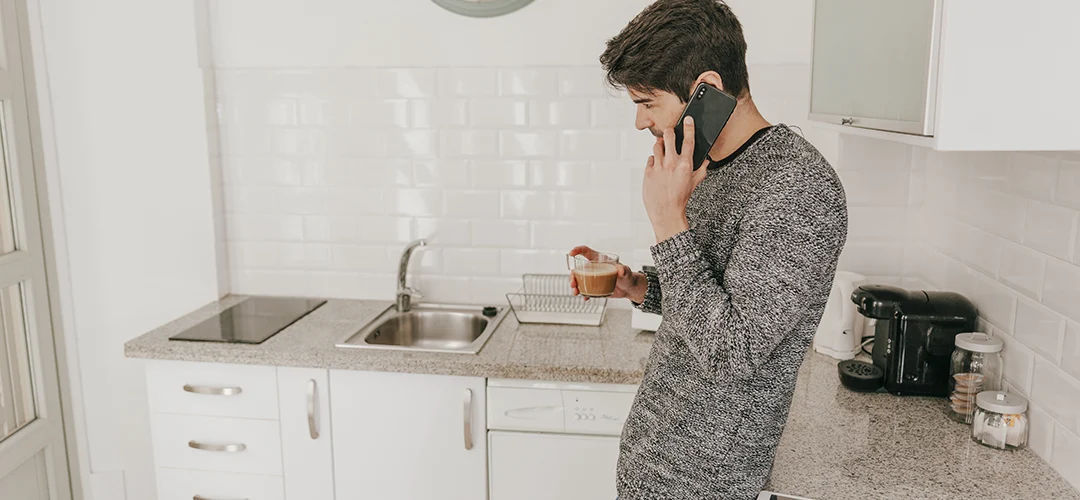 Man in een keuken die een loodgieter belt omdat de gootsteen verstopt is.
