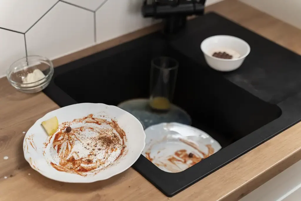 Schmutziges Geschirr und Speisereste in einer Spüle, die zu verstopfen droht.